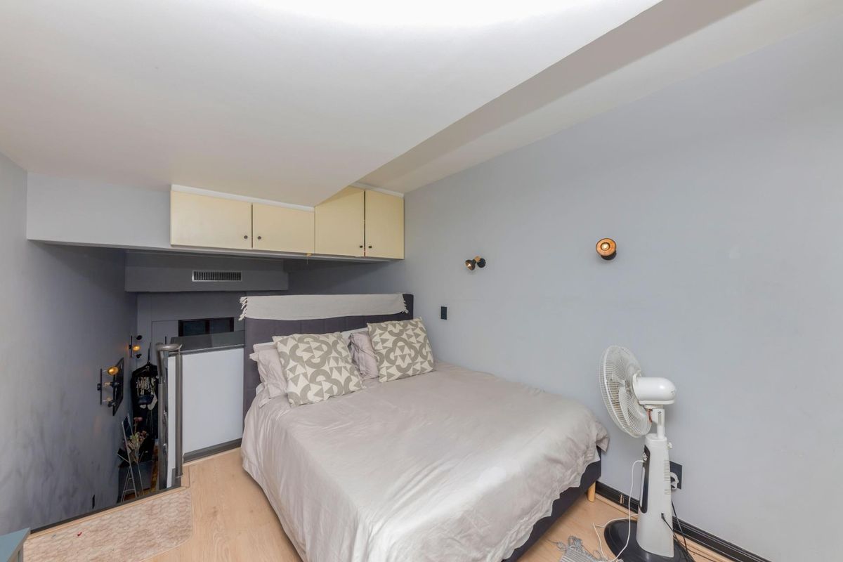 A compact bedroom featuring built-in overhead storage cabinets, light wood-look flooring, and wall-mounted lighting fixtures.