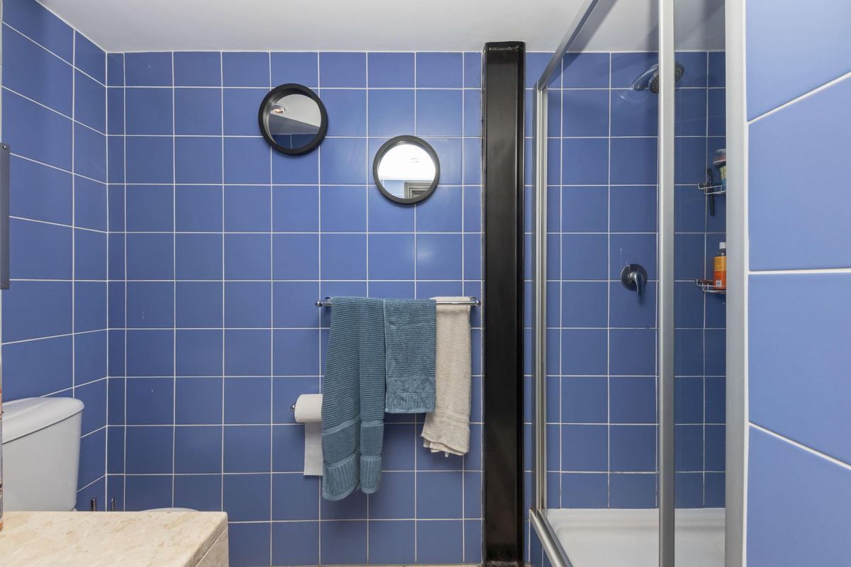 A functional bathroom featuring blue wall tiles, a glass-enclosed shower, and a standard toilet suite.