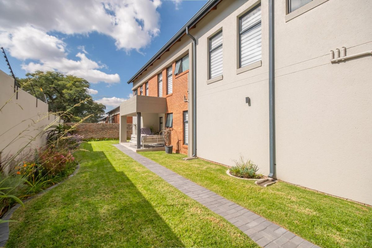 A view of the rear exterior of the house, featuring a paved walkway, a small covered patio area, and a well-maintained lawn.