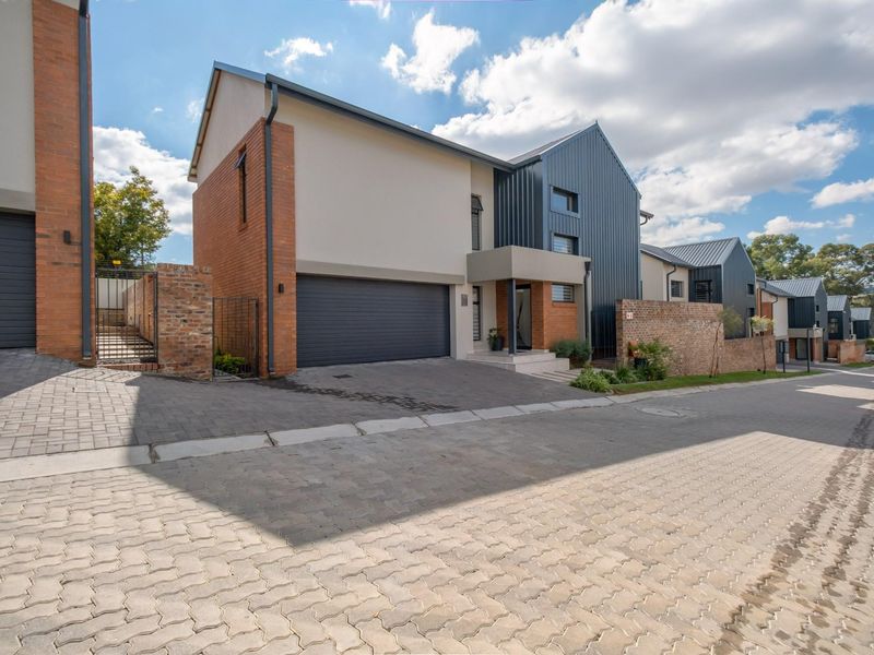 Modern double-story residential townhouse featuring a brick and metal facade, paved driveway, and integrated double garage within a secure estate setting.