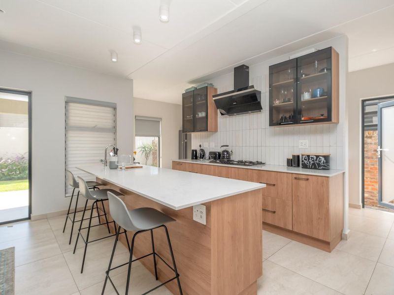 Modern kitchen featuring light wood cabinetry, stone countertops, a central island with breakfast bar seating, and integrated stainless steel appliances.