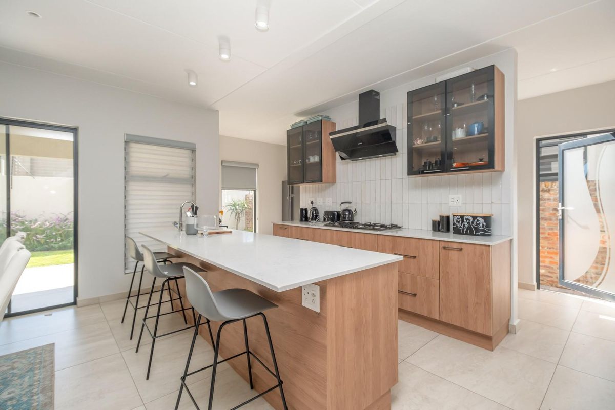 Modern kitchen featuring light wood cabinetry, stone countertops, a central island with breakfast bar seating, and integrated stainless steel appliances.