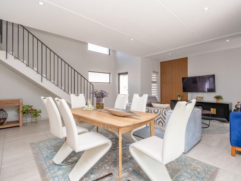 Spacious open-plan living and dining area featuring modern tiled flooring, recessed ceiling lighting, and a contemporary staircase with metal balustrades.