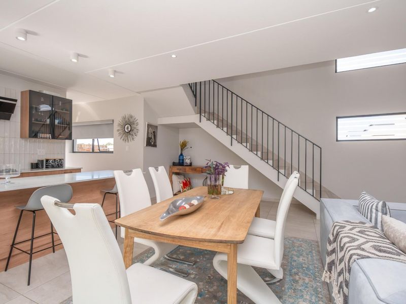 Modern open-plan living area featuring a contemporary kitchen with breakfast bar, dining space, and a staircase with sleek metal railings.