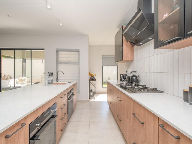 Modern kitchen featuring light wood cabinetry, stone countertops, a central island, built-in oven, gas hob, and sleek extractor fan with direct patio access.