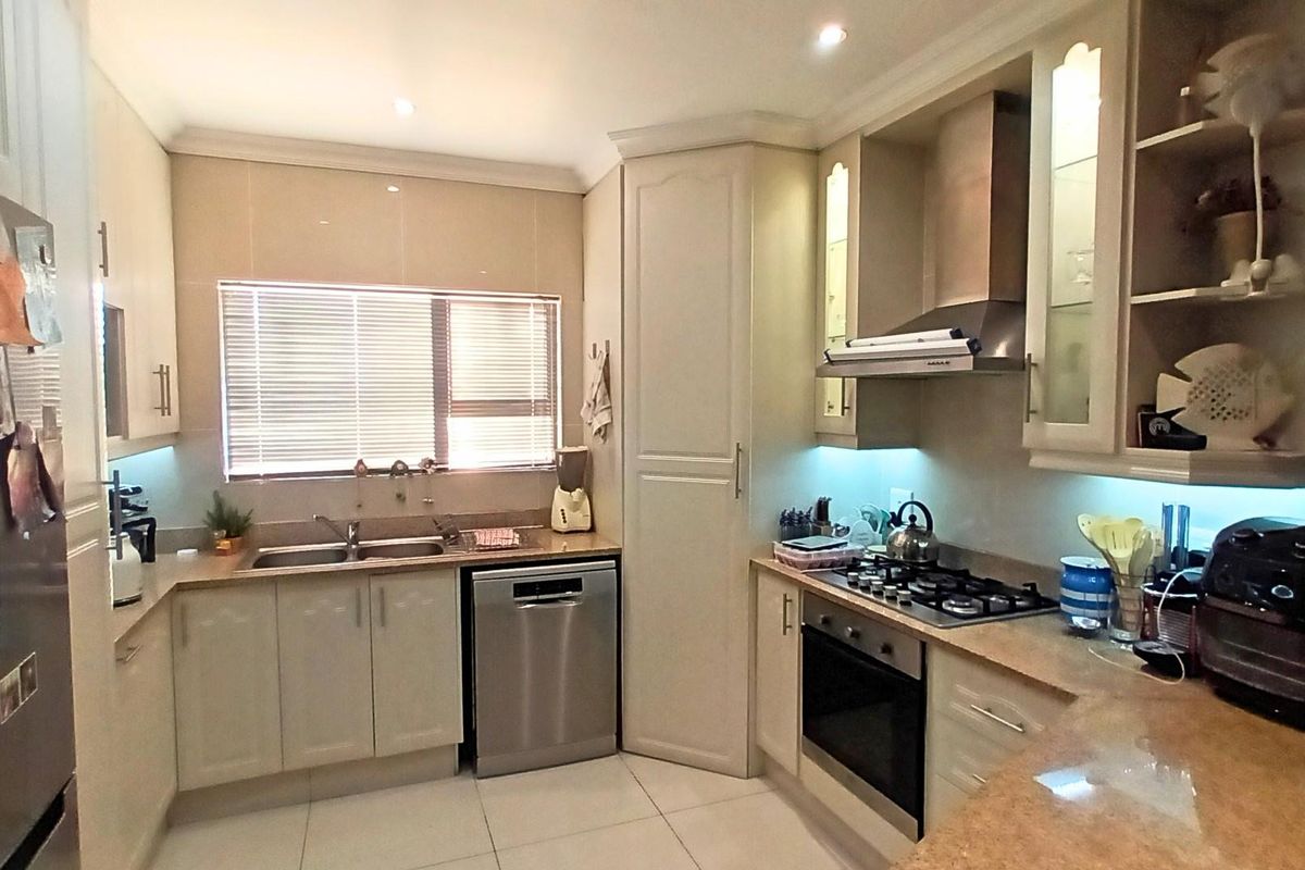 A well-appointed kitchen featuring built-in cabinetry, a gas hob, extractor fan, integrated oven, double sink, and tiled flooring with under-cabinet lighting.