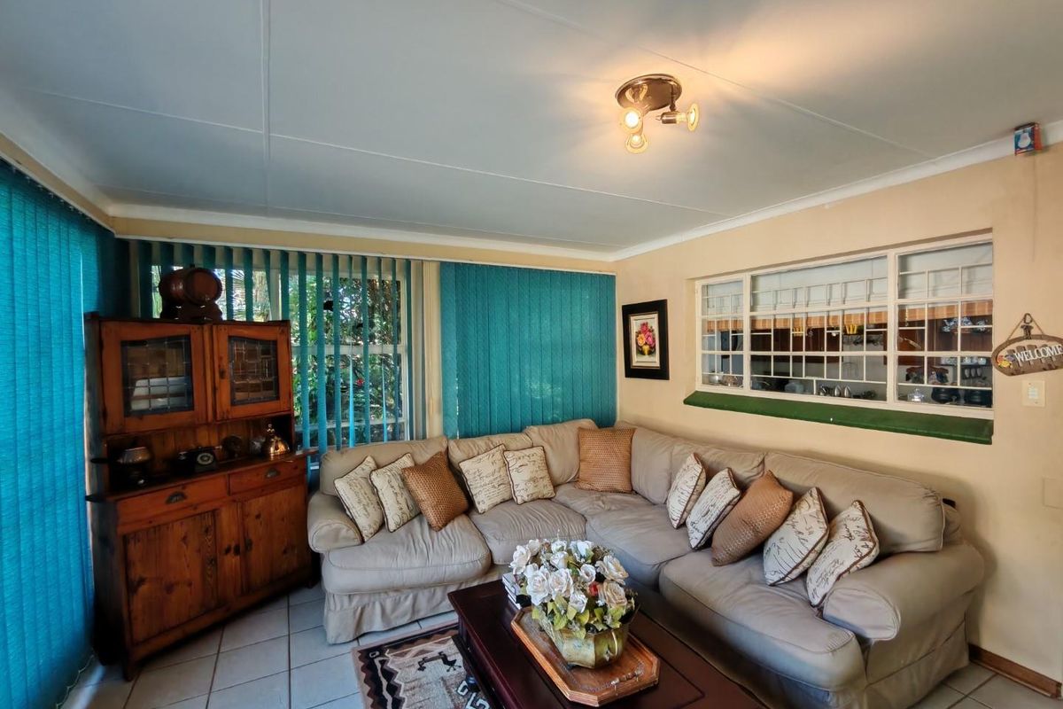 A cozy living room featuring tiled flooring, vertical blinds, and a serving hatch window connecting to the kitchen area.
