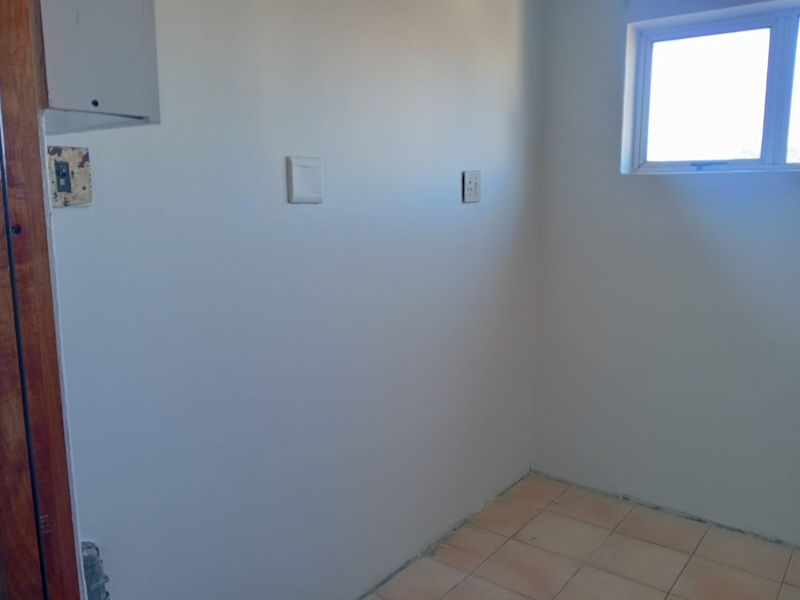 A small, empty utility or laundry space featuring tiled flooring, a window, and basic electrical points, ready for customization.