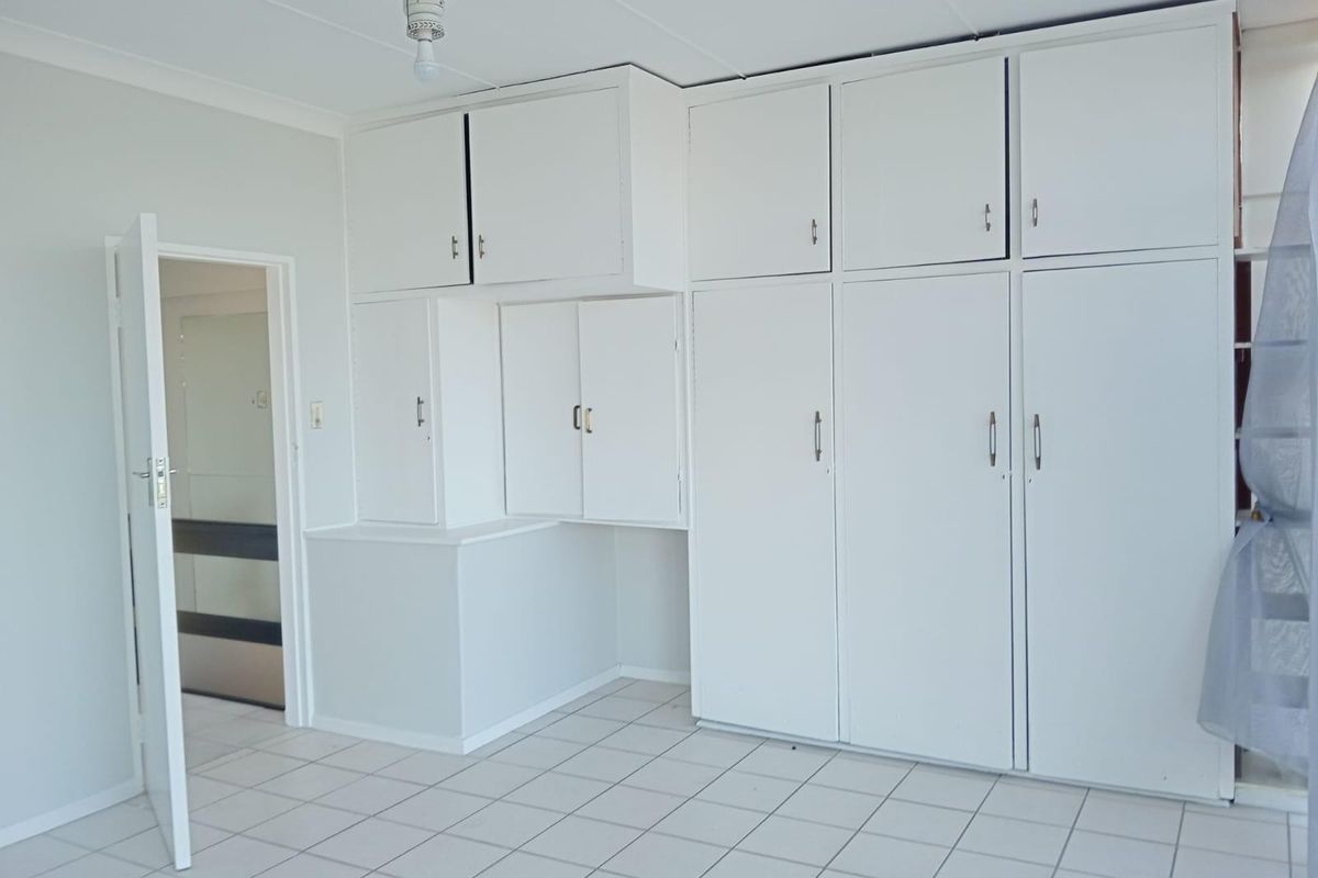 A bedroom featuring extensive built-in white cabinetry with overhead storage and tiled flooring, offering ample storage space.