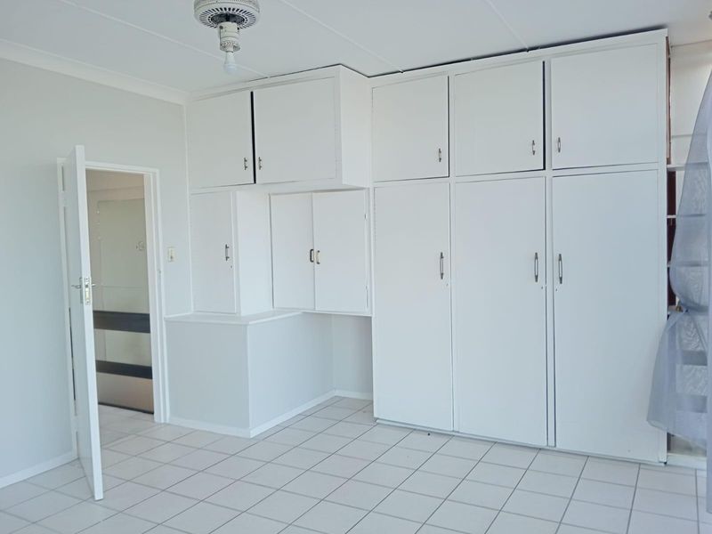 A bedroom featuring extensive built-in white cabinetry with overhead storage and tiled flooring, offering ample storage space.