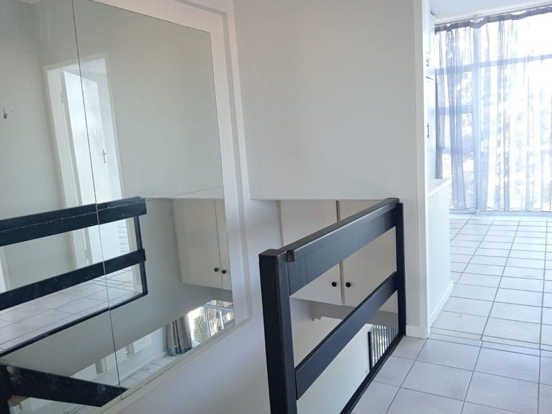 A bright hallway area featuring tiled flooring, a built-in mirror, and a dark-toned safety railing overlooking the lower level.