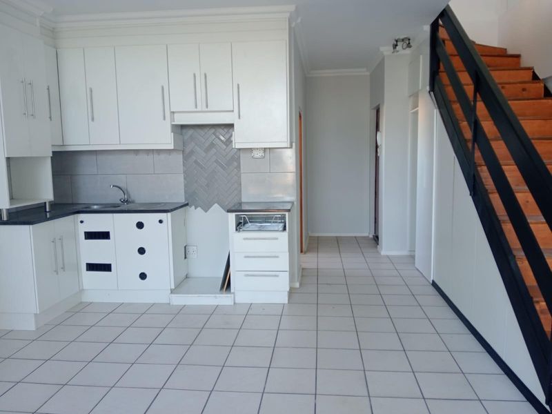 Open plan kitchen featuring white cabinetry, dark countertops, and tiled flooring, adjacent to a staircase leading to the upper level.