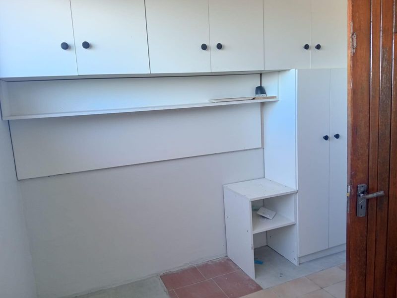 A functional utility space or study area featuring built-in white cabinetry, overhead storage, and a dedicated desk unit.