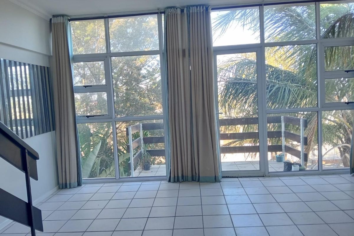 Bright living area featuring large floor-to-ceiling windows and glass doors leading to a private balcony, with neutral tiled flooring throughout.