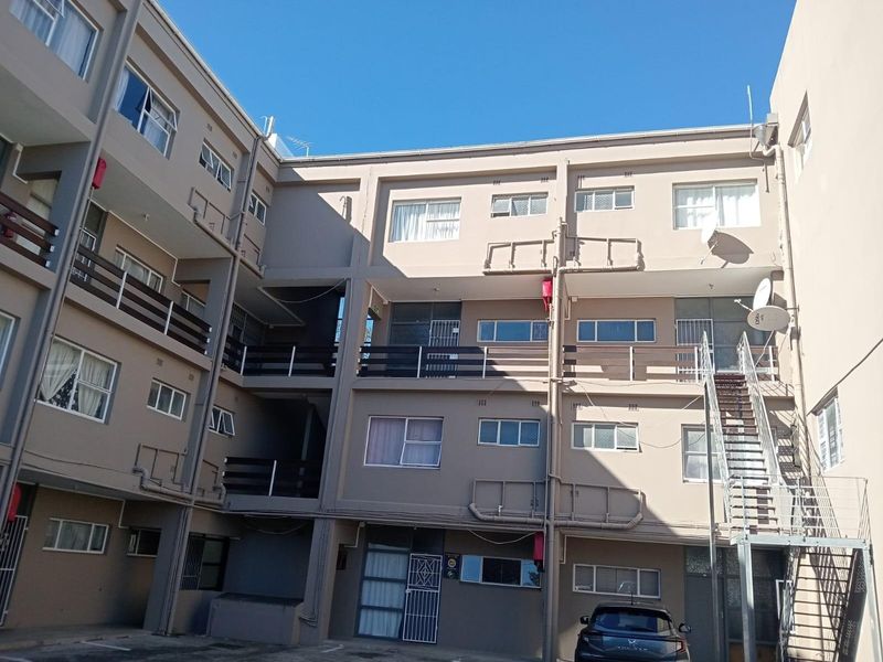 Exterior view of a multi-story apartment complex featuring balconies, external staircases, and a paved courtyard area.