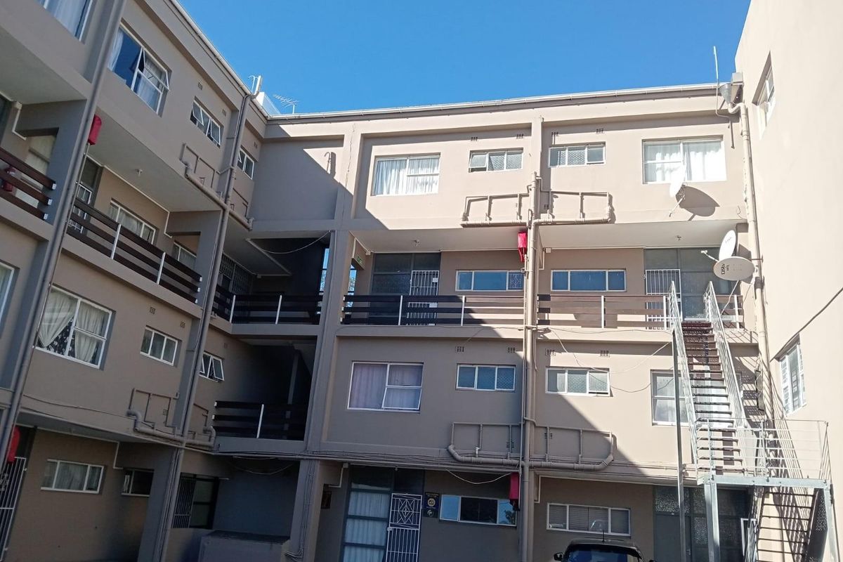 Exterior view of a multi-story apartment complex featuring balconies, external staircases, and a paved courtyard area.