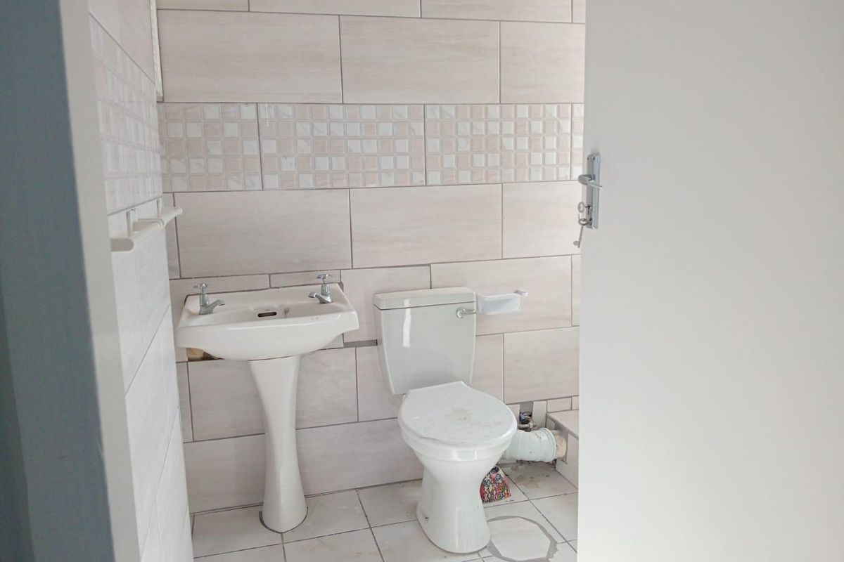 A compact bathroom featuring a pedestal basin and toilet with neutral wall tiling and tiled flooring.