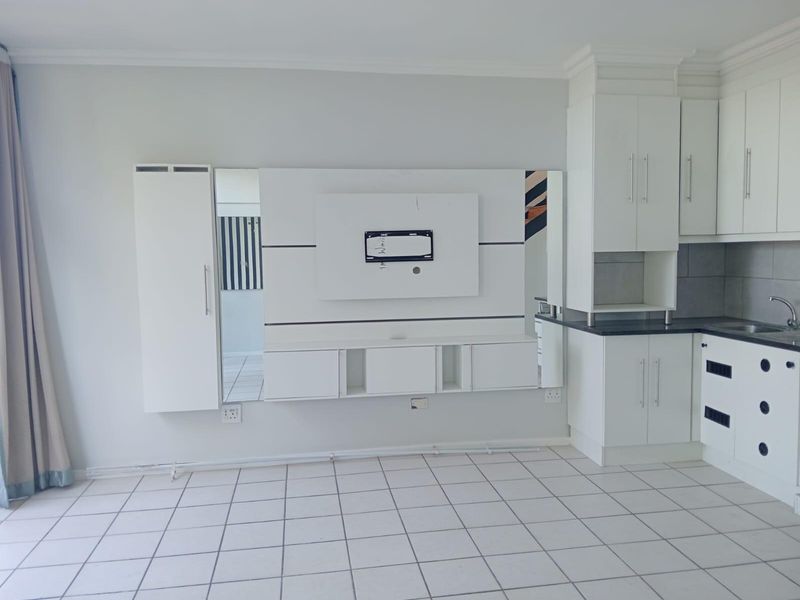 An open-plan living and kitchen area featuring white cabinetry, a built-in media unit, and tiled flooring throughout.