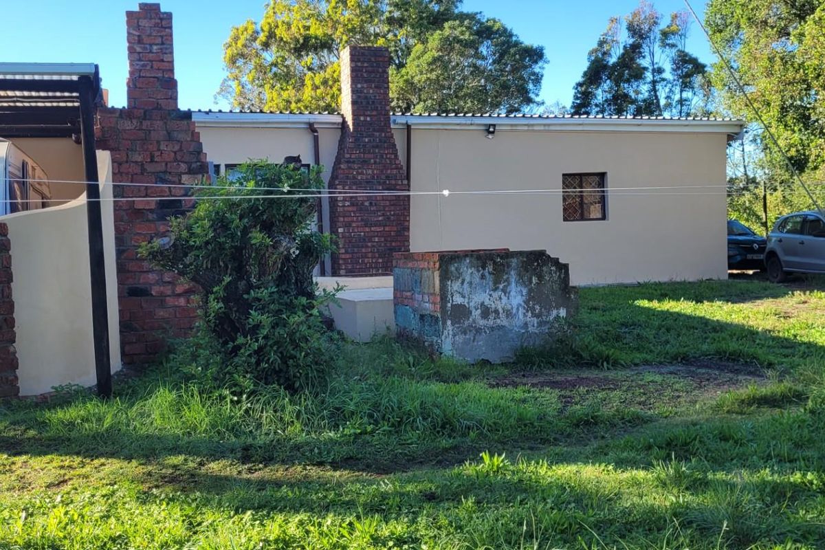 Rear exterior view of the farm property featuring a brick chimney, covered parking area, and an outdoor masonry structure set within a large garden.