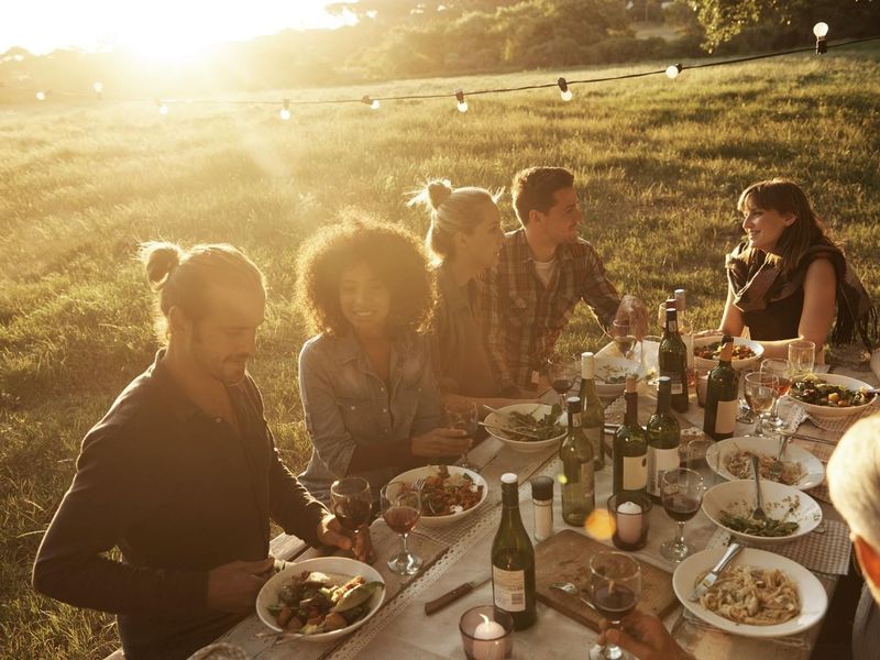 An outdoor dining setting in a grassy field at sunset, featuring string lights and a rustic table arrangement.