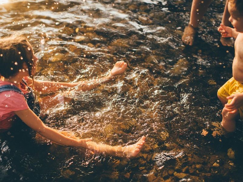 A candid shot of children playing in a shallow water feature or natural stream, highlighting the outdoor recreational potential of the property.