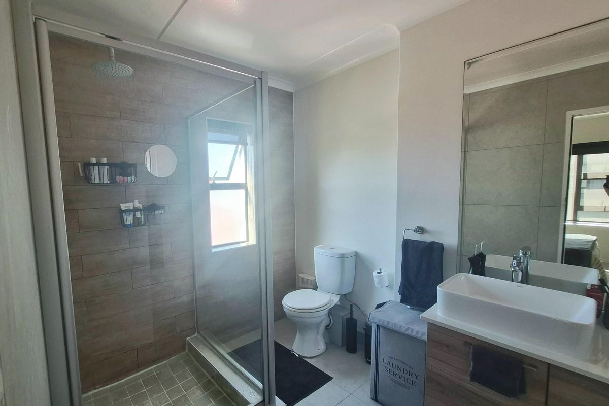 Modern bathroom featuring a glass-enclosed shower with wood-look tiling, a contemporary vanity with a vessel sink, and a standard toilet.