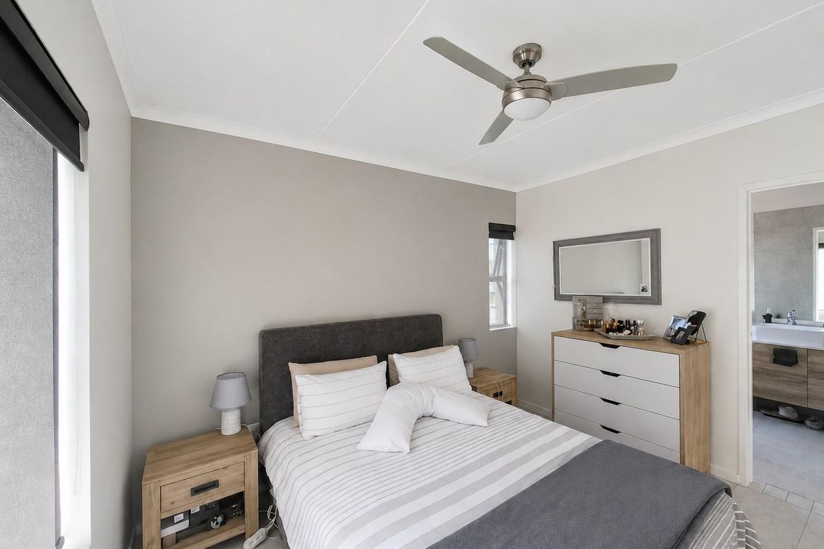 A well-maintained bedroom featuring a ceiling fan, neutral wall tones, and an adjoining en-suite bathroom with modern finishes.
