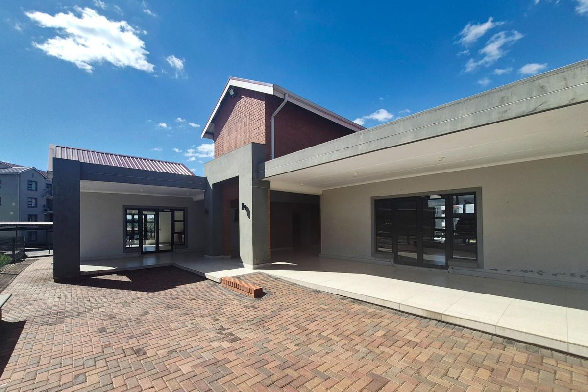 Spacious paved courtyard area featuring a covered patio, modern brick and plaster facade, and large glass sliding doors providing access to the interior.