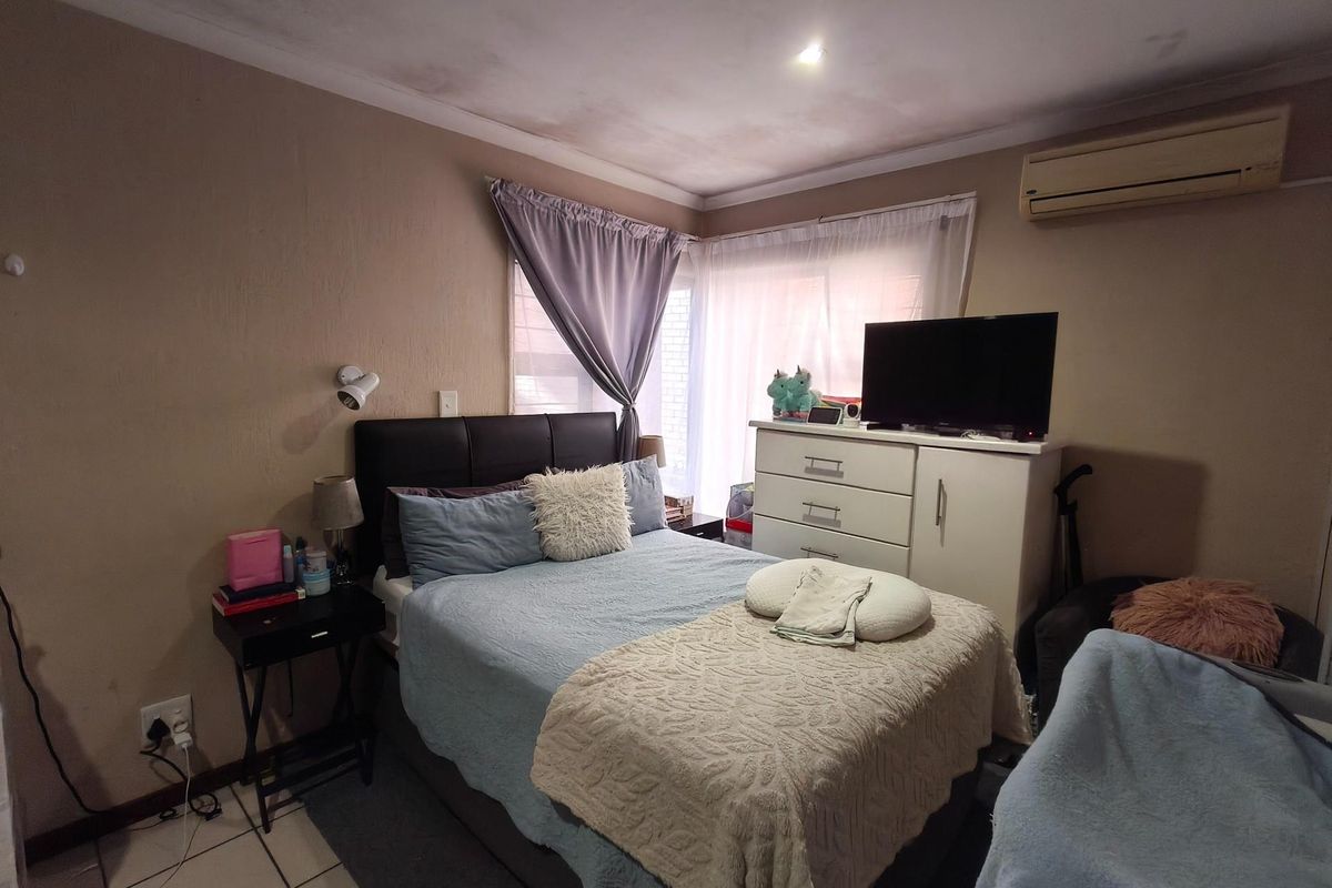 A bedroom featuring tiled flooring, a wall-mounted air conditioning unit, and corner windows providing natural light.