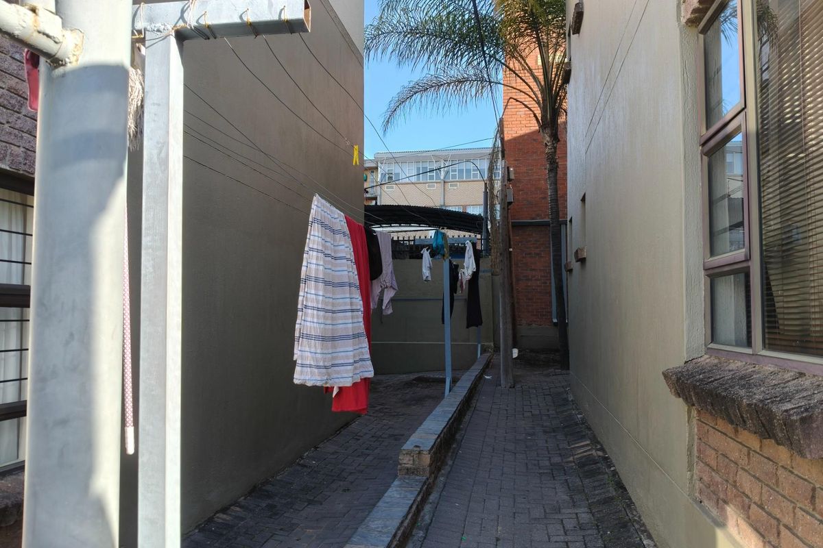 A narrow exterior side passage featuring paved flooring and a metal washing line structure between two building walls.