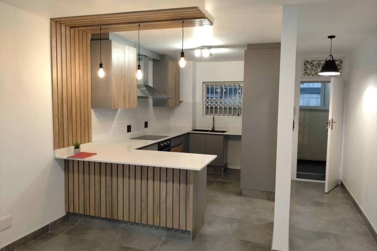 Modern kitchen featuring sleek grey cabinetry, white stone countertops, timber slat detailing, and integrated stainless steel appliances, creating a contemporary and functional culinary space.
