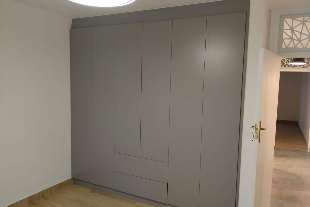 A bedroom featuring modern, floor-to-ceiling built-in grey cabinetry with integrated drawers and light wood-look flooring.