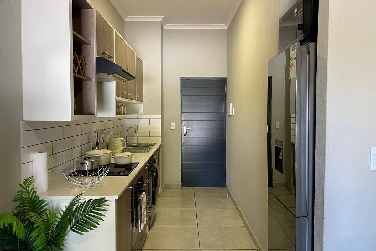 A modern, compact kitchen featuring sleek cabinetry, subway tile backsplash, integrated hob, and tiled flooring, leading to a secure entrance door.