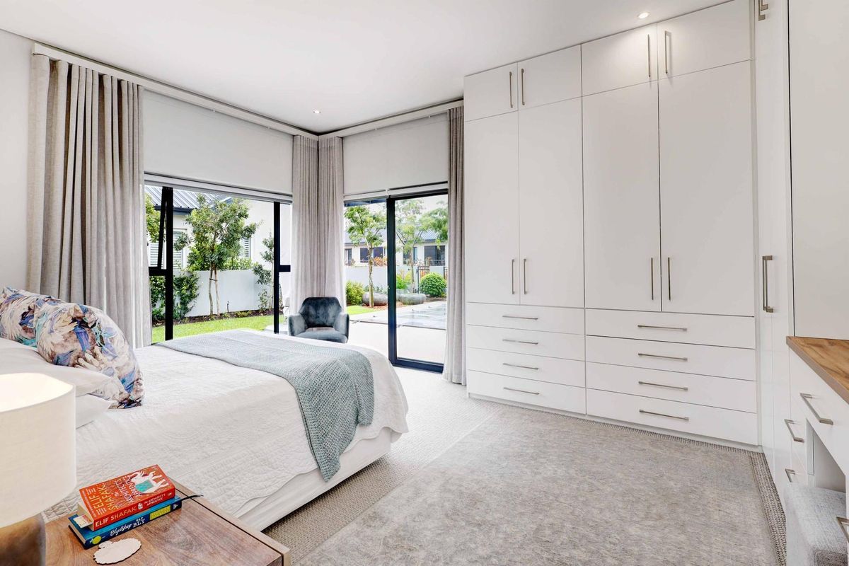 Spacious bedroom featuring extensive built-in cabinetry, neutral carpeting, and large sliding glass doors providing direct access to the garden area.
