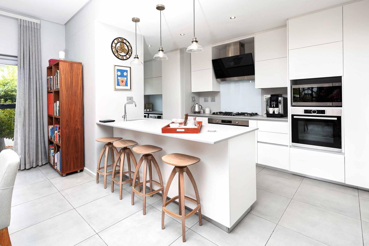 Modern kitchen featuring a central island with breakfast bar, sleek white cabinetry, integrated appliances, and high-quality tiled flooring.