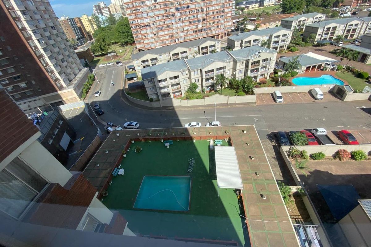 Aerial view of the apartment complex featuring a communal swimming pool, paved terrace area, and surrounding residential buildings with street-level parking.