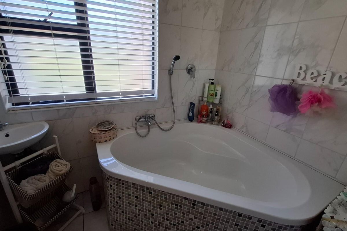 A functional bathroom featuring a corner bathtub with wall-mounted shower mixer, basin, and tiled wall finishes.