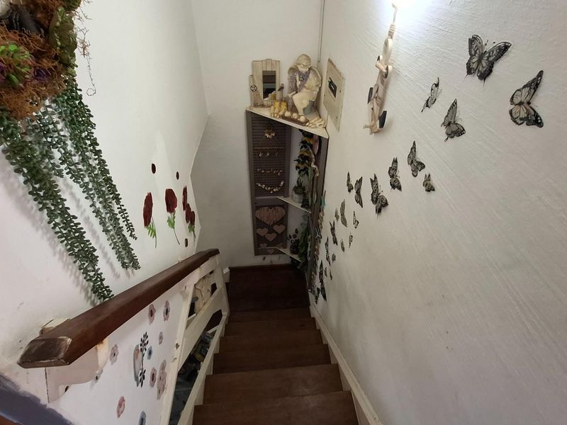 A staircase hallway featuring wooden steps and a handrail, leading to a lower level with a built-in corner shelving unit.