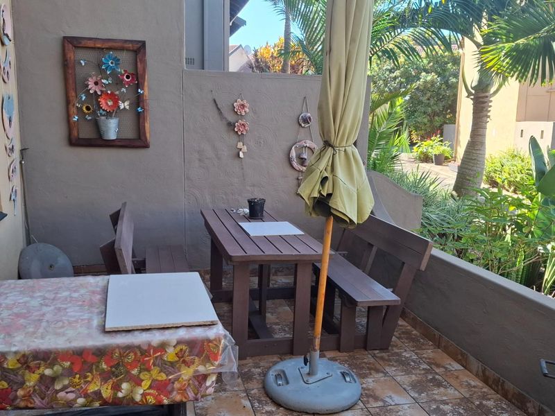 A covered outdoor patio area featuring tiled flooring and a low perimeter wall, providing a functional space for outdoor dining and relaxation.