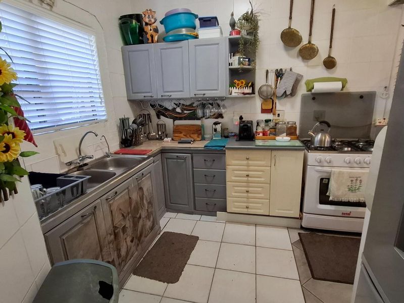 A compact kitchen featuring a gas stove, double basin sink, tiled splashback, and a mix of grey and cream cabinetry.