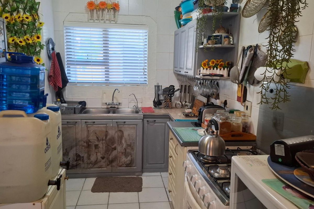 A compact kitchen featuring built-in cabinetry, a double basin sink, and a gas hob, with tiled flooring and a window with venetian blinds.