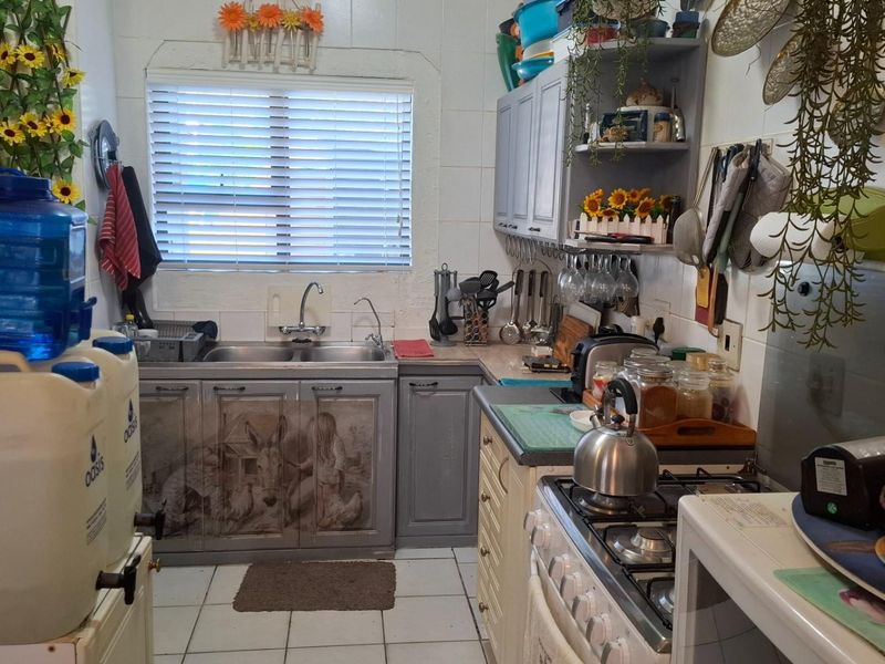 A compact kitchen featuring built-in cabinetry, a double basin sink, and a gas hob, with tiled flooring and a window with venetian blinds.