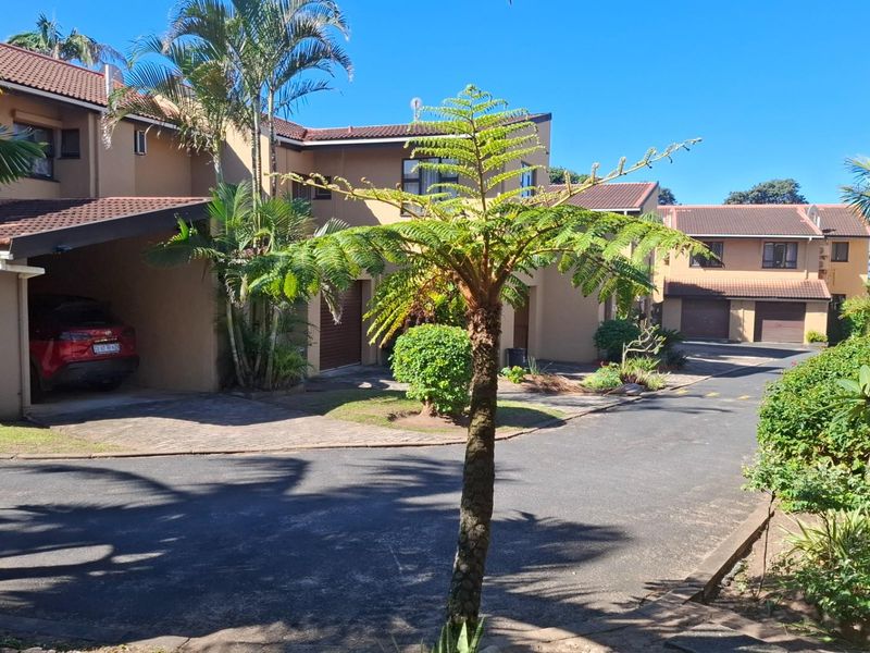 Exterior view of a residential apartment complex featuring paved driveways, carports, and garage access within a landscaped setting.