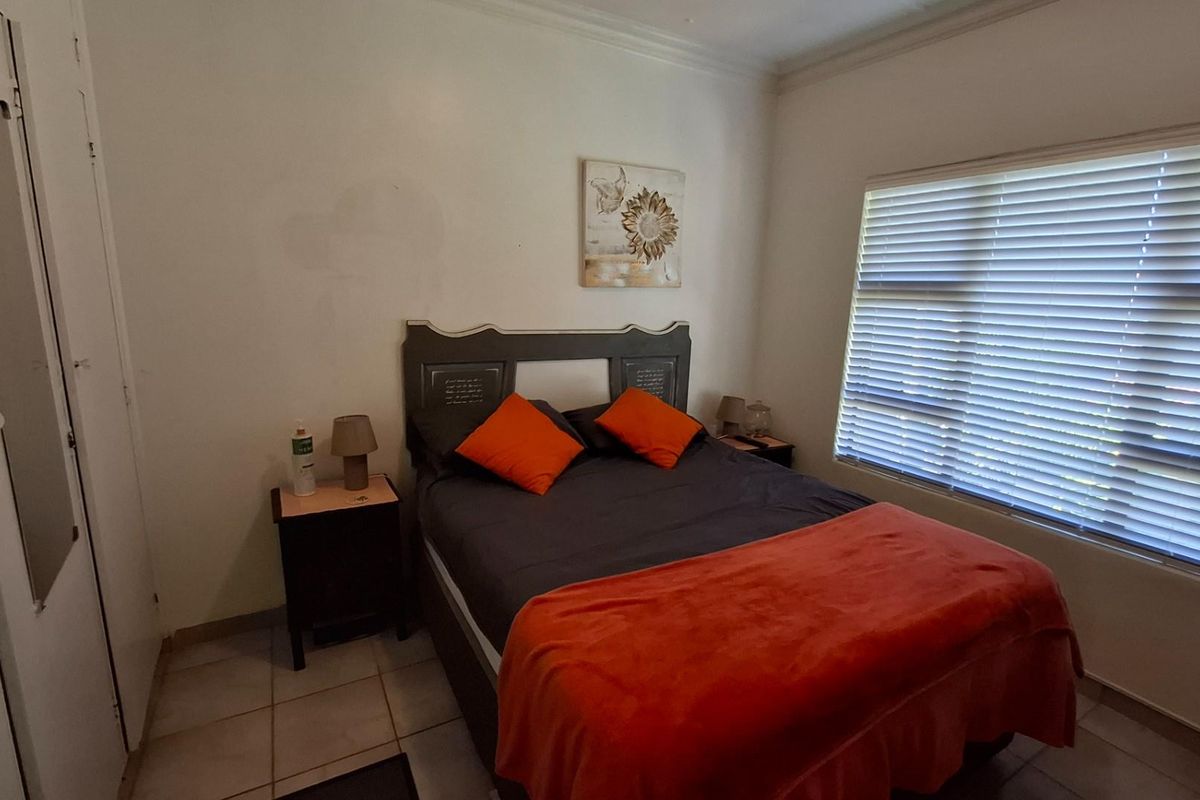 A functional bedroom featuring tiled flooring, built-in cupboards, and venetian blinds, providing a neutral base for potential interior updates.