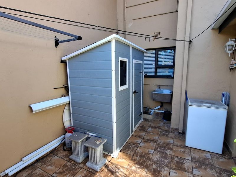 A rear exterior courtyard area featuring tiled flooring, a wall-mounted washing line, and an external utility sink.