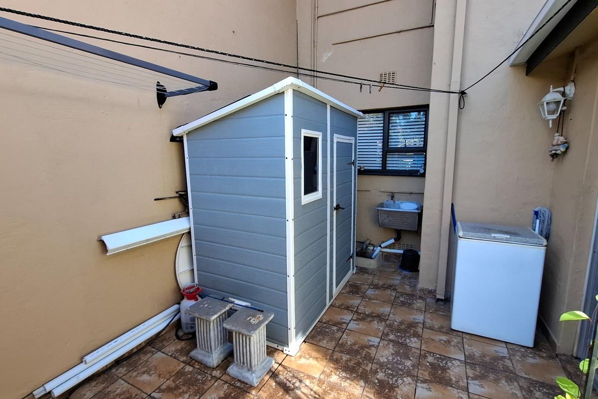 A rear exterior courtyard area featuring tiled flooring, a wall-mounted washing line, and an external utility sink.