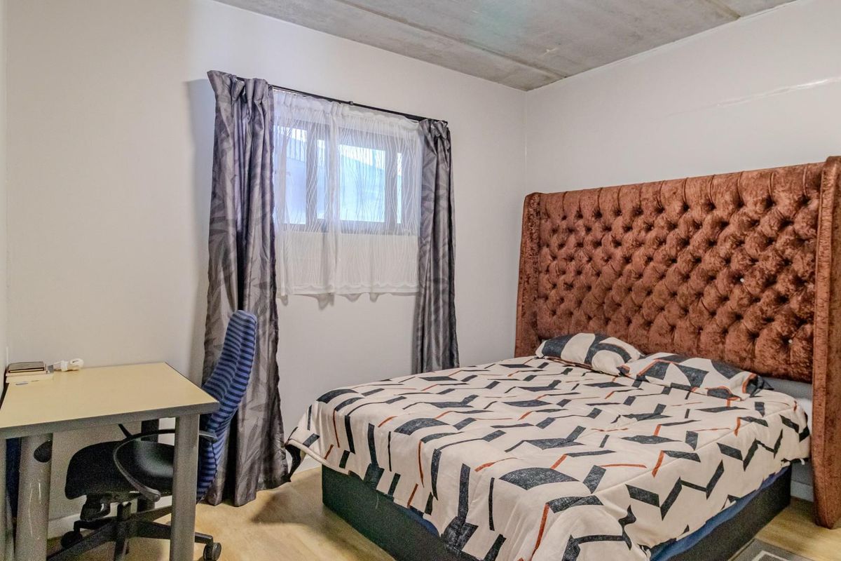 A bedroom featuring a tufted headboard, light wood-look flooring, and an exposed concrete ceiling, providing a modern industrial aesthetic.