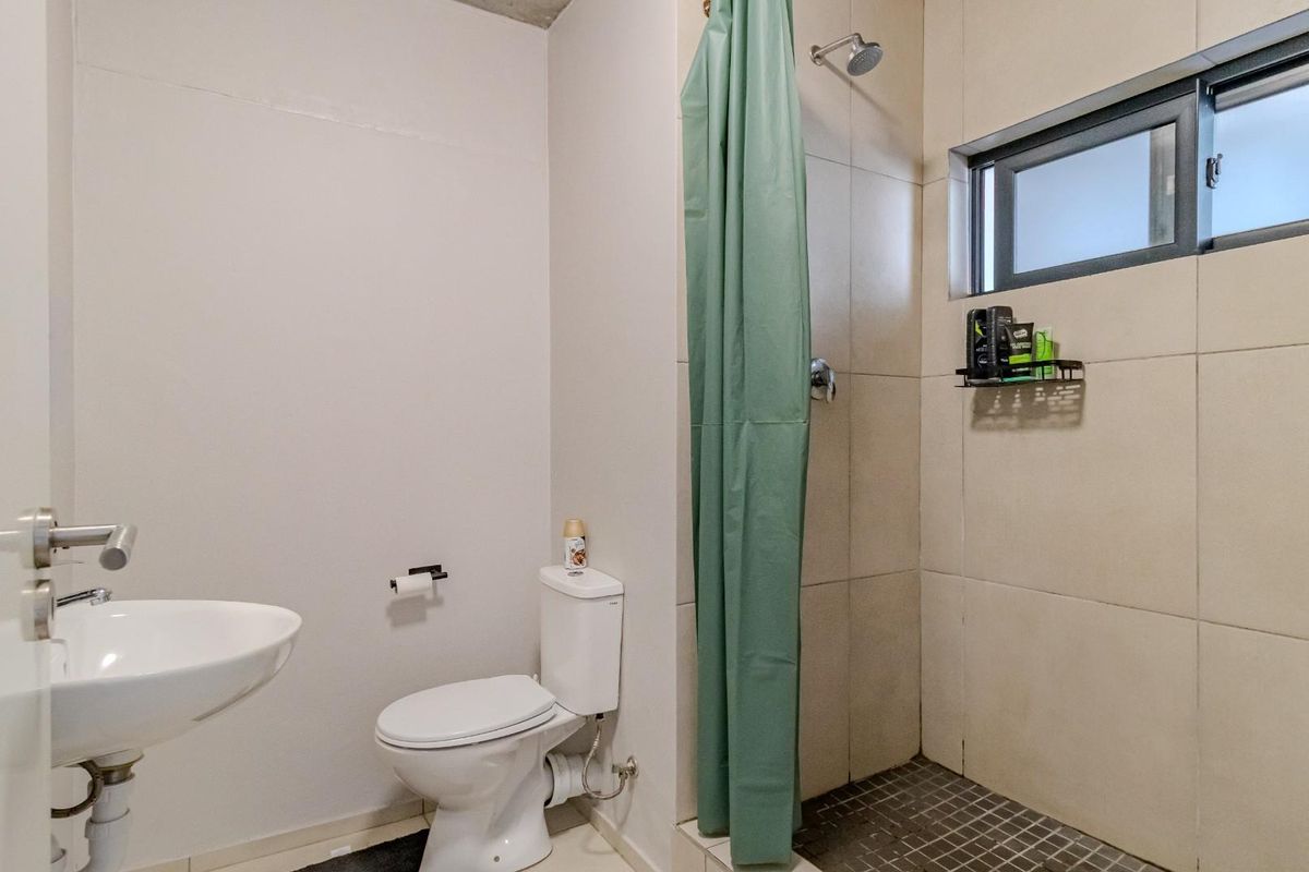 A functional bathroom featuring a wall-mounted basin, a standard toilet, and a tiled shower enclosure with a window for natural ventilation.