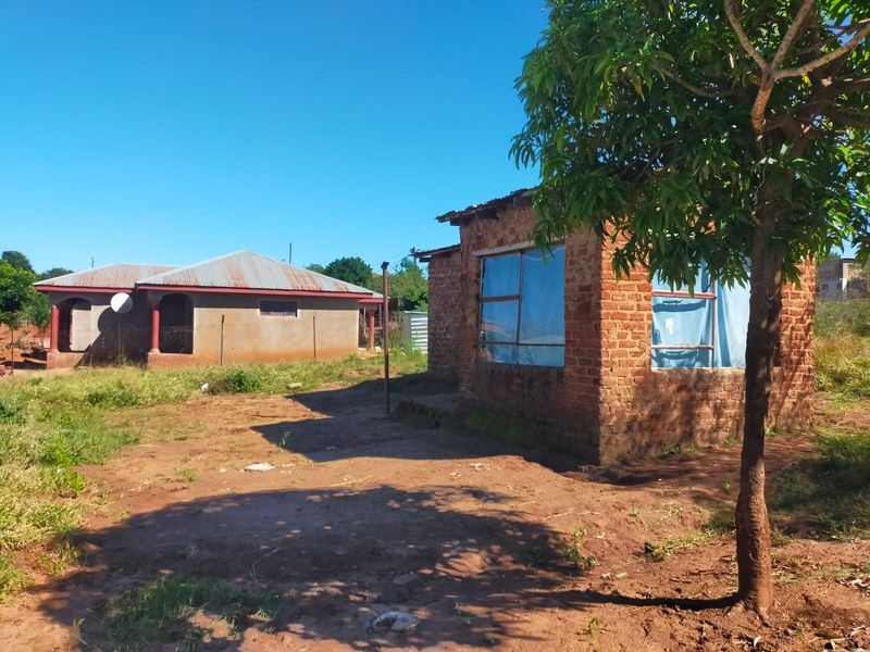 A view of a residential property featuring an unfinished brick structure and a secondary dwelling on a large, unlandscaped plot of land.