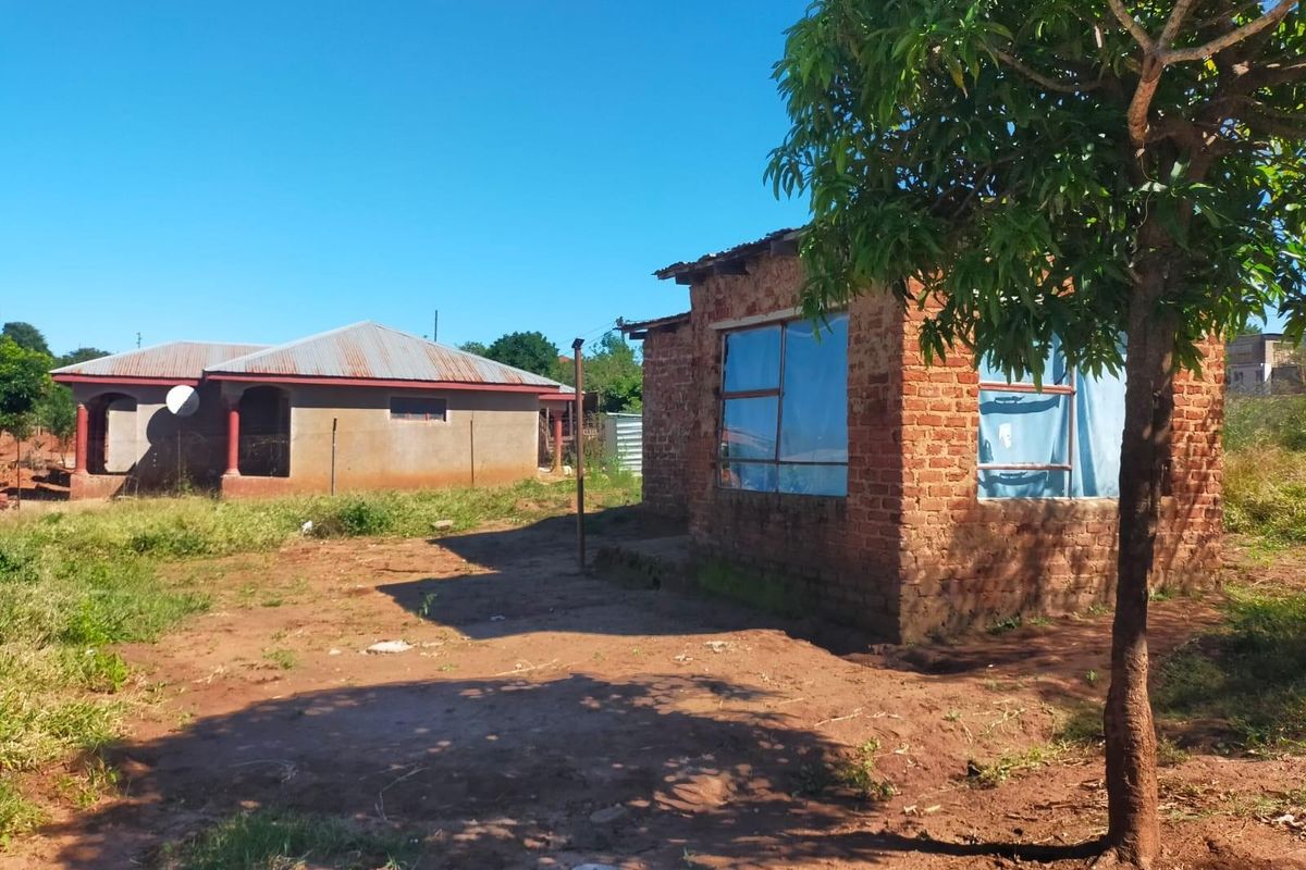 A view of a residential property featuring an unfinished brick structure and a secondary dwelling on a large, unlandscaped plot of land.